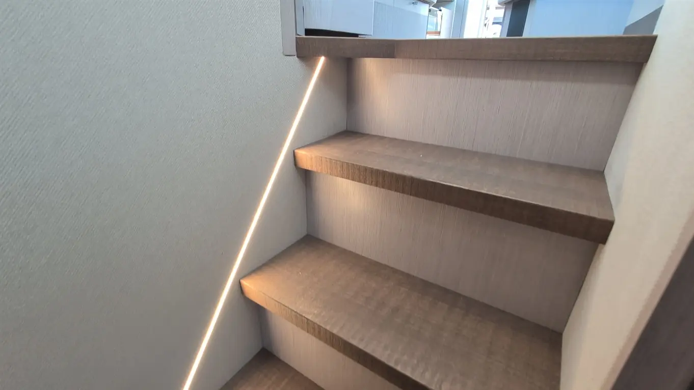 Modern wooden stairs with LED strip lighting, leading to an upper level in a well-lit interior space.